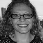 Black and white photo of a woman in glasses smiling to the camera